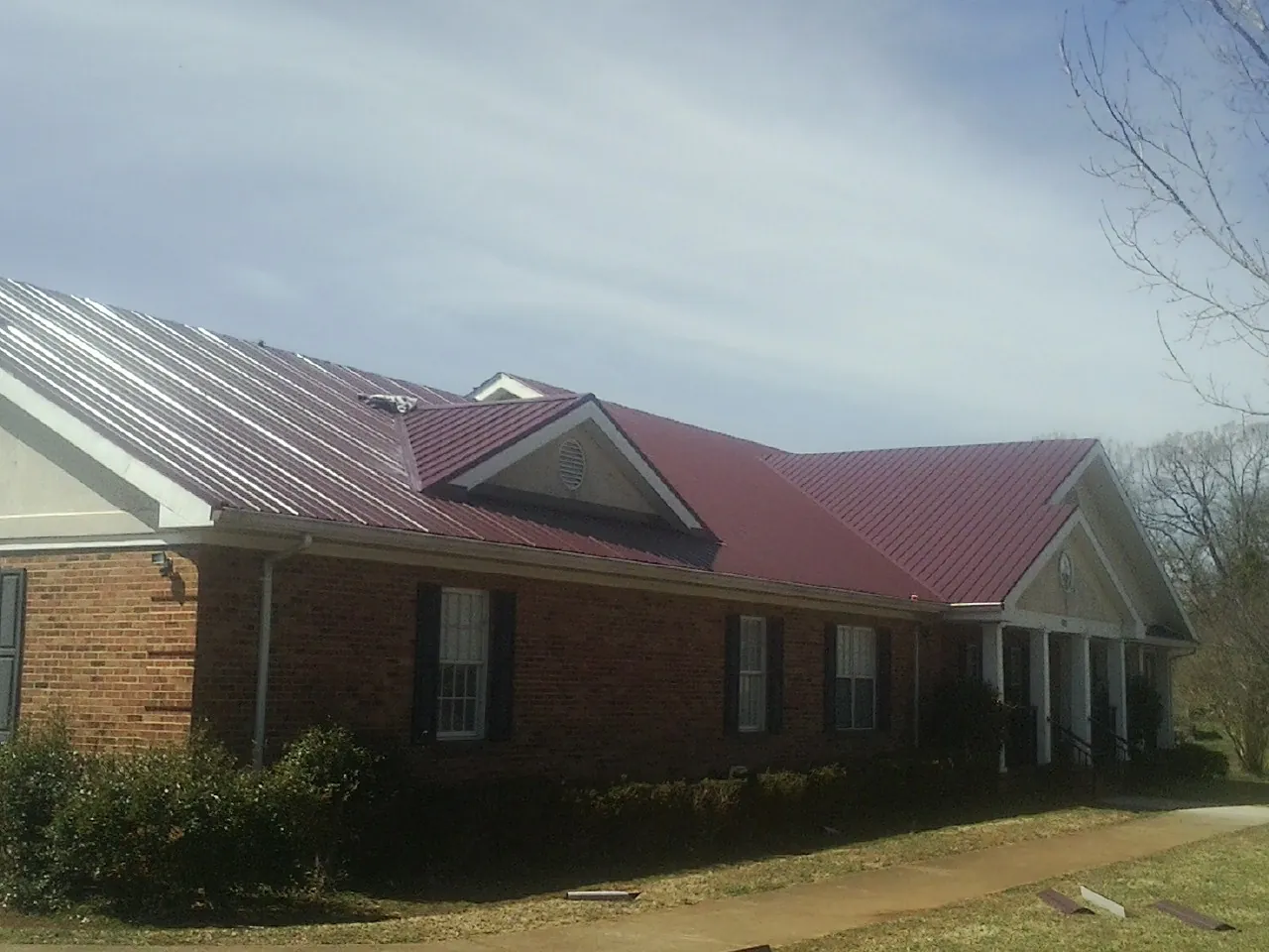 Red metal roof with gabled entries on a long brick building, from a Hail Damage Roof Repair job in Greenacres