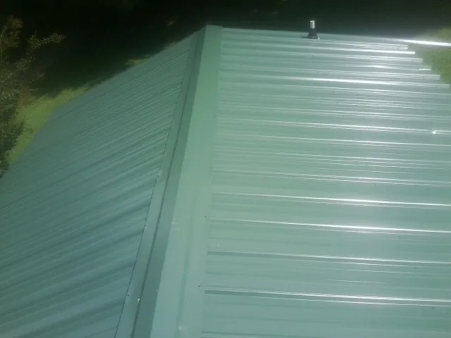 New green metal panels meeting at the ridge of a roof — Flat Roof Repair work by our crew in Greenacres