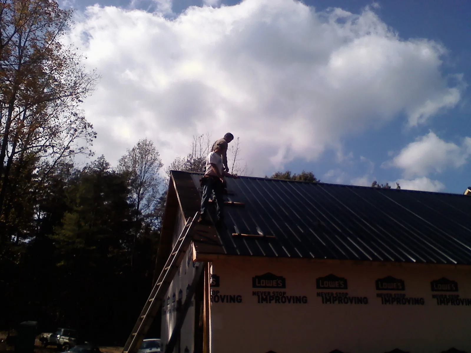 Roofer fastening dark metal panels high against a cloudy sky, from a Roof Inspection job in Greenacres