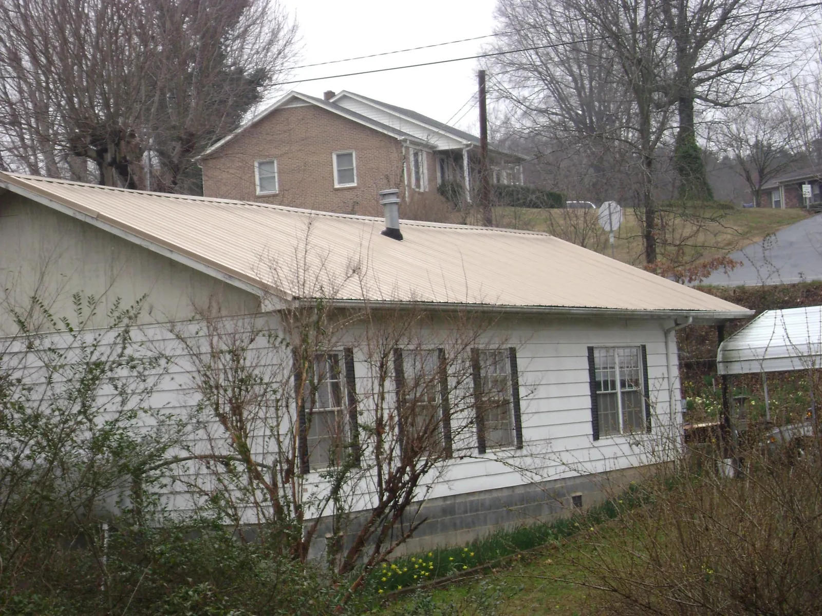 Tan metal roof on a white sided house set into a hillside — Commercial Roofing by Roofing Brothers in Greenacres