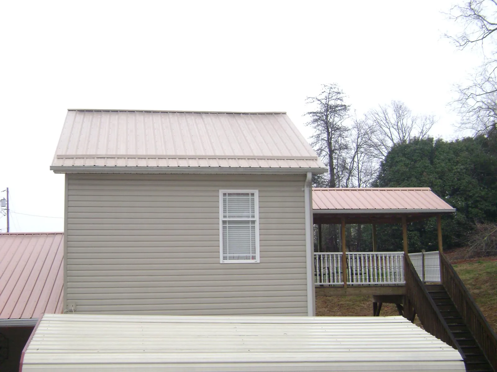 Tan metal roofs on a two story addition and attached porch, from a Roof Replacement job in Greenacres